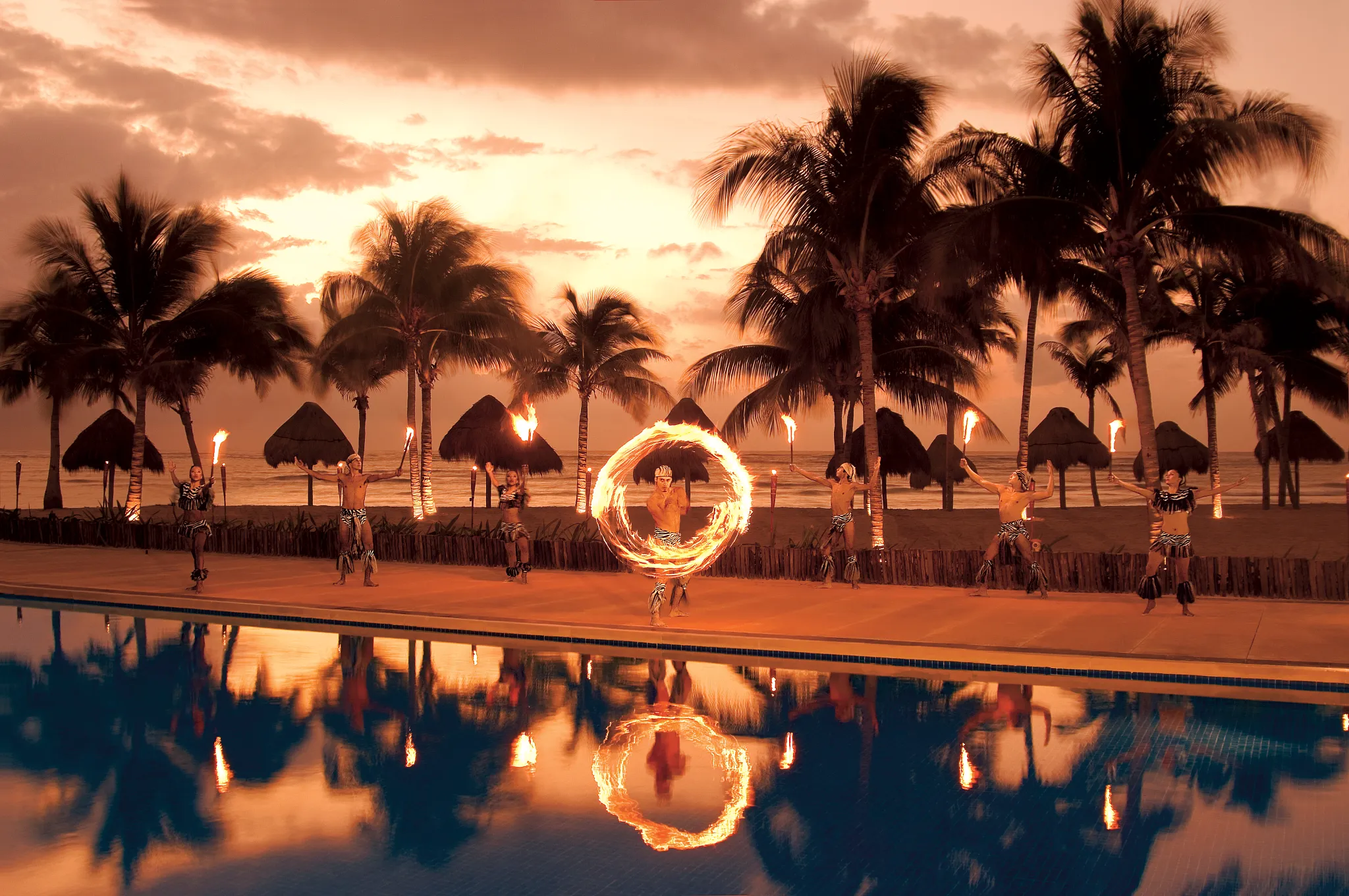 Fire performers entertaining guests beside the pool at sunset at Dreams Tulum Resort & Spa in Riviera Maya.