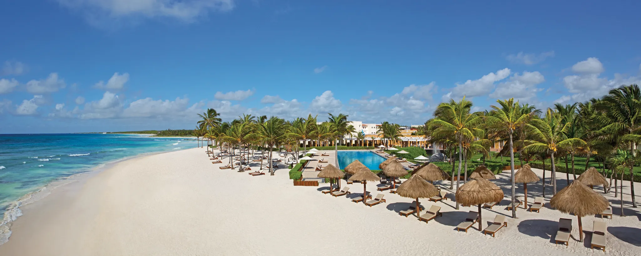 Panoramic beachfront view with palapas and lounge chairs at Dreams Tulum Resort & Spa.