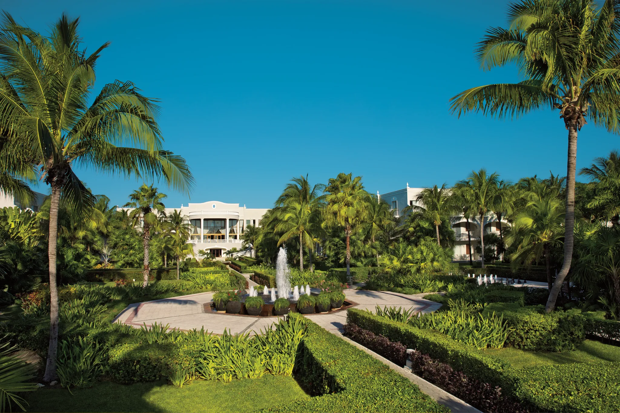 Lush tropical gardens and elegant fountain courtyard at Dreams Tulum Resort & Spa, surrounded by palm trees and colonial-style architecture.