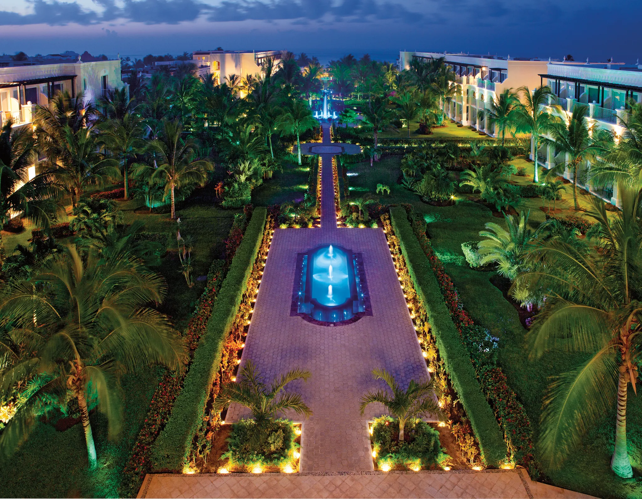 Tropical gardens illuminated at night at Dreams Tulum Resort & Spa with pathways, fountains, and palm trees
