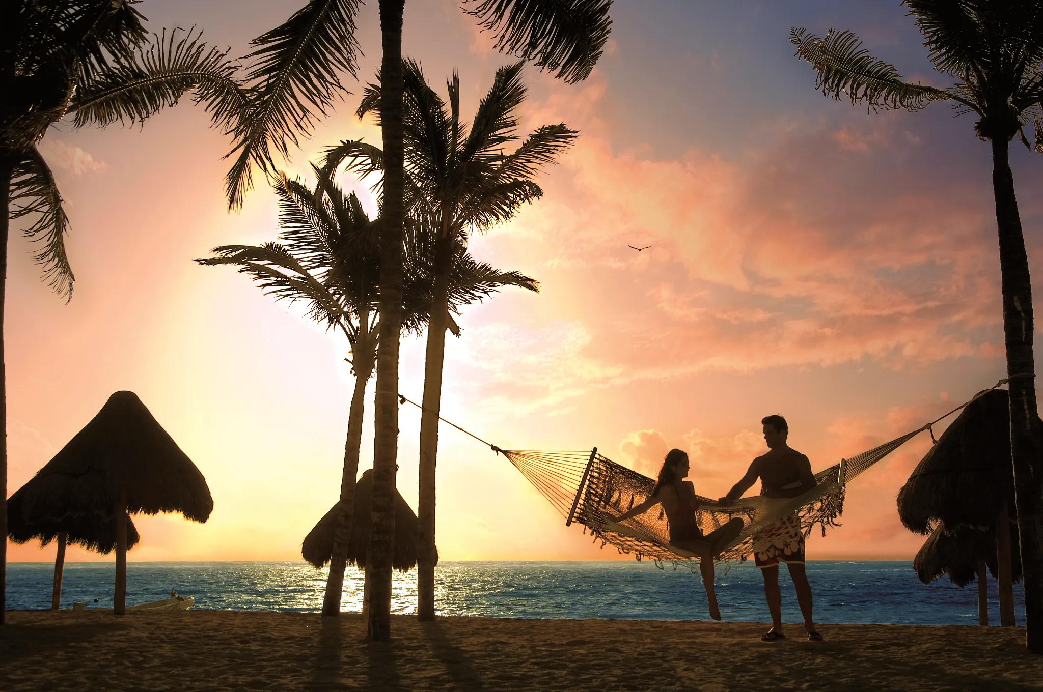 Couple relaxing in a hammock at sunset on the beach at Dreams Tulum Resort & Spa in Riviera Maya.